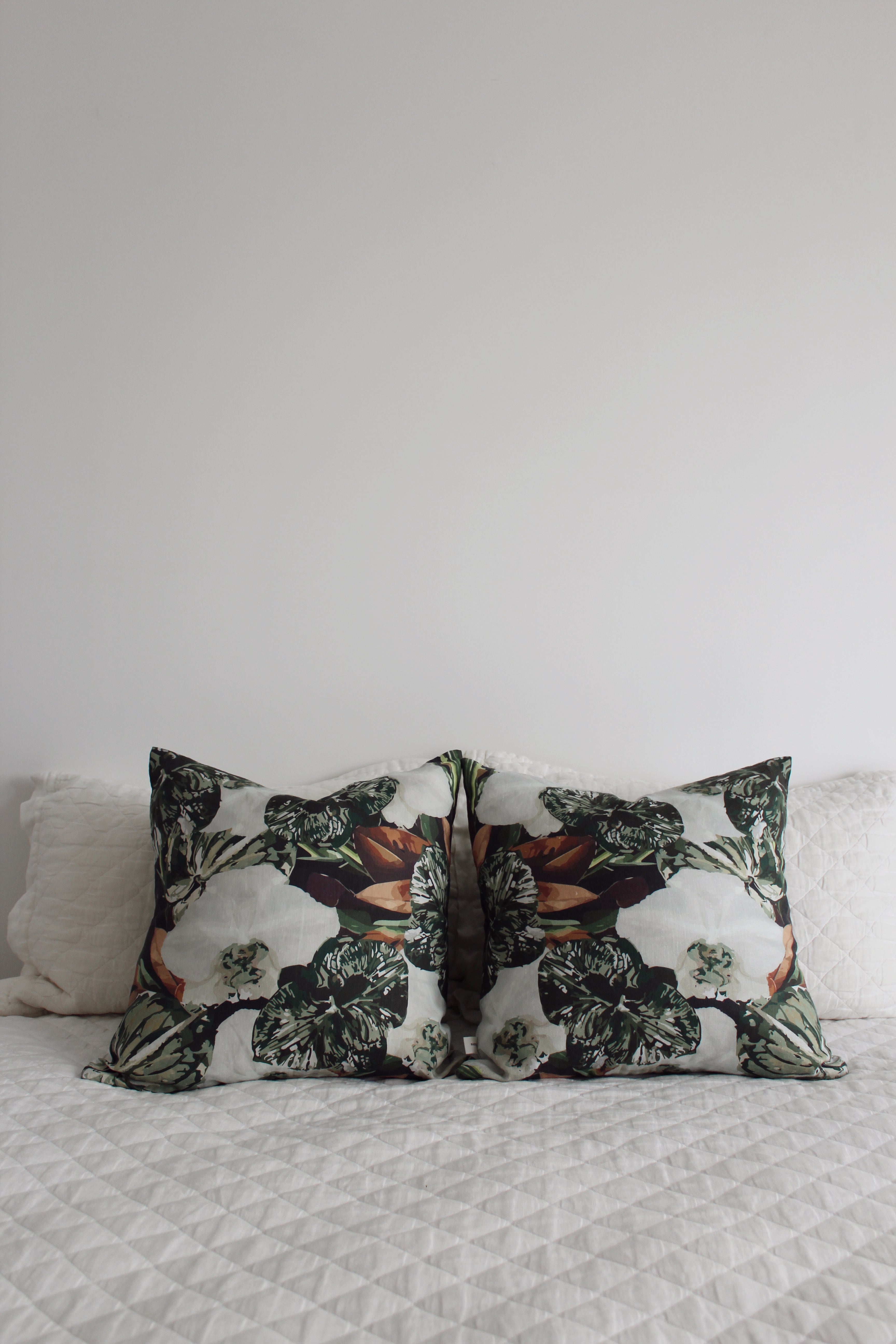Pistachio green floral cushions paired and styled on white linen bedding